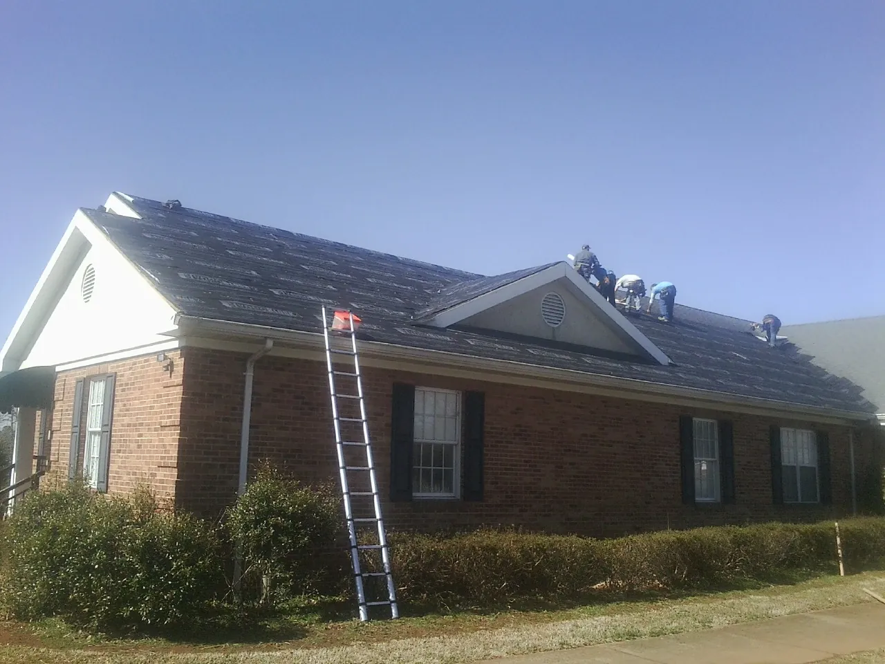 Crew tearing shingles off a brick ranch roof with a ladder set — Emergency Roof Repair work by our crew in Hercules