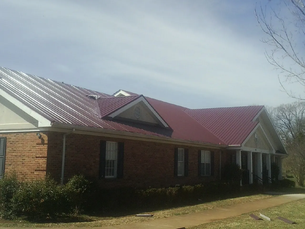 Red metal roof with gabled entries on a long brick building, from a Hail Damage Roof Repair job in Hercules