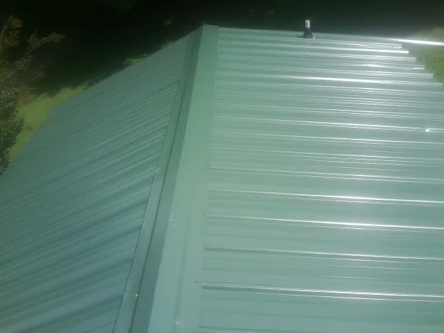 New green metal panels meeting at the ridge of a roof — Flat Roof Repair work by our crew in Hercules